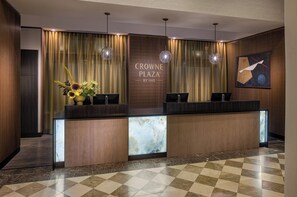 A reception desk with a marble top, two black chairs, a floral arrangement, and a sign reading "CROWNE PLAZA BY IHG".