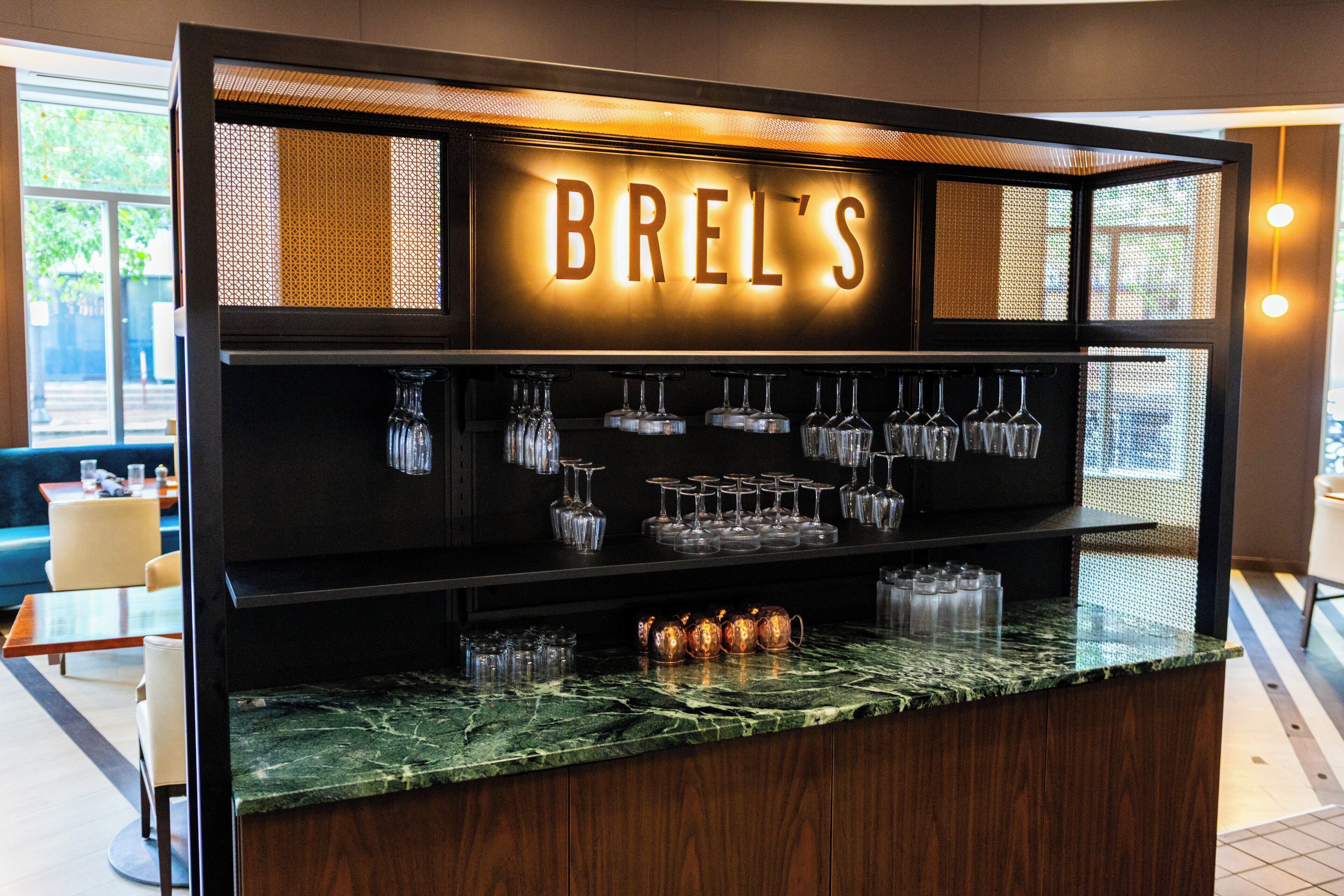 Zona de bar con letrero iluminado 'BREL'S', copas de vino y botellas en estantes.