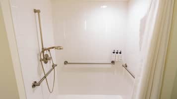 A modern bathroom with white tiles, a shower with a handheld showerhead, and a grab bar.