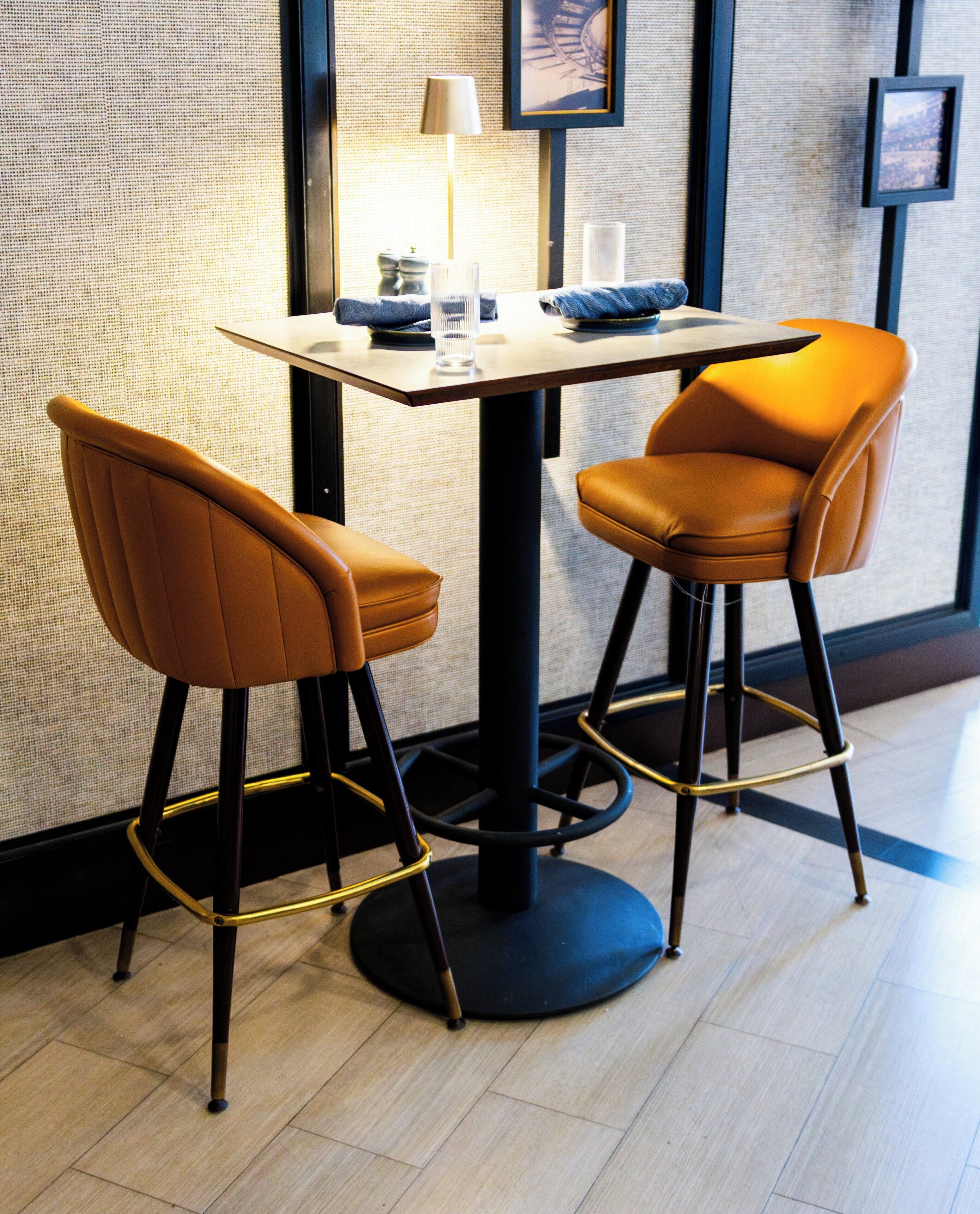 Eine moderne Bar mit zwei hohen Barhocker und einem Tisch, inklusive einer Lampe und Dekorationselementen.