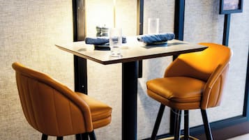 Eine moderne Bar mit zwei hohen Barhocker und einem Tisch, inklusive einer Lampe und Dekorationselementen.