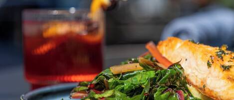Ein Teller mit Lachs und Grünzeug, dazu ein Glas roter Saft mit einer Zitronenscheibe.