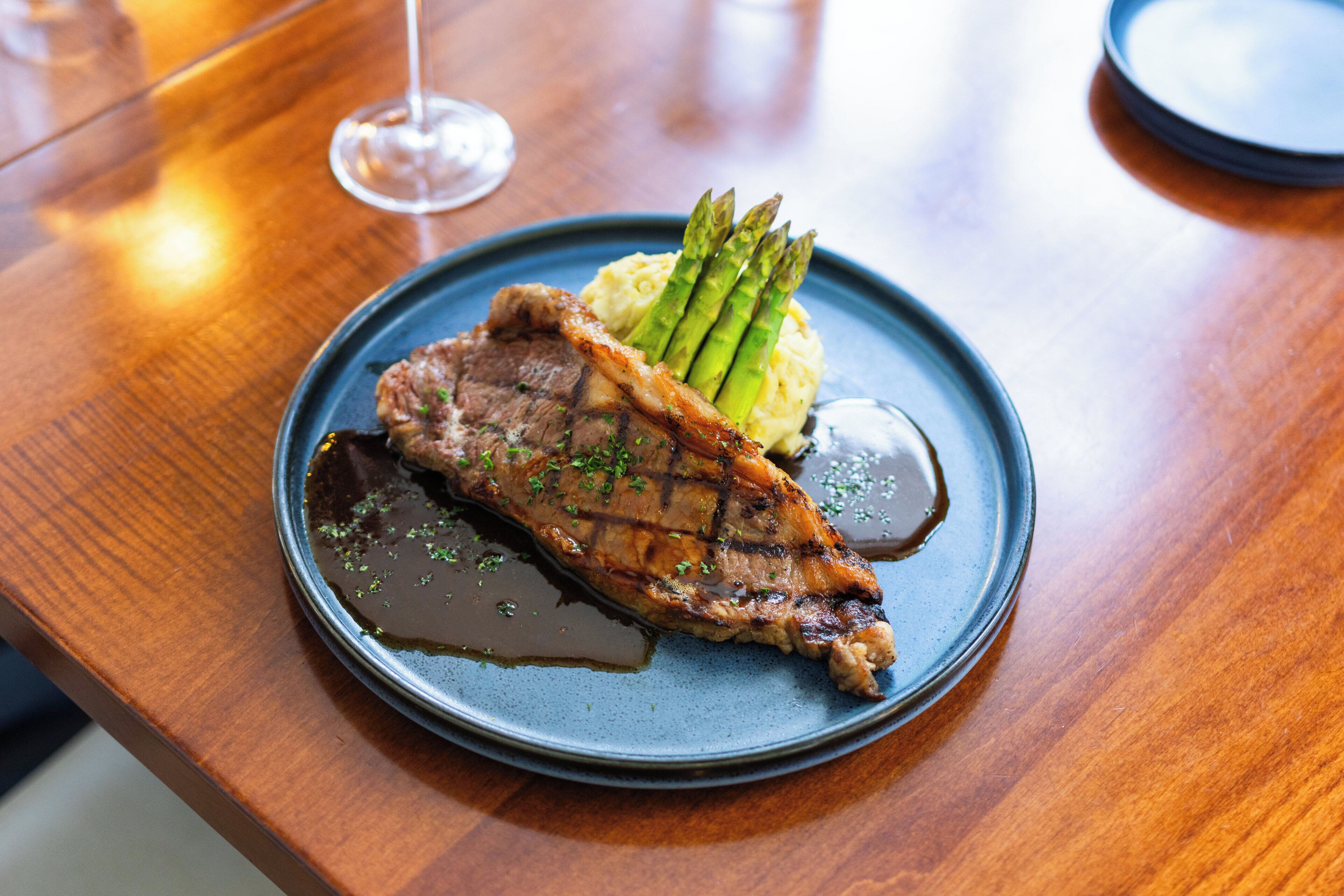 Une assiette contenant un steak, des asperges et de la purée de pommes de terre, posée sur une table en bois.