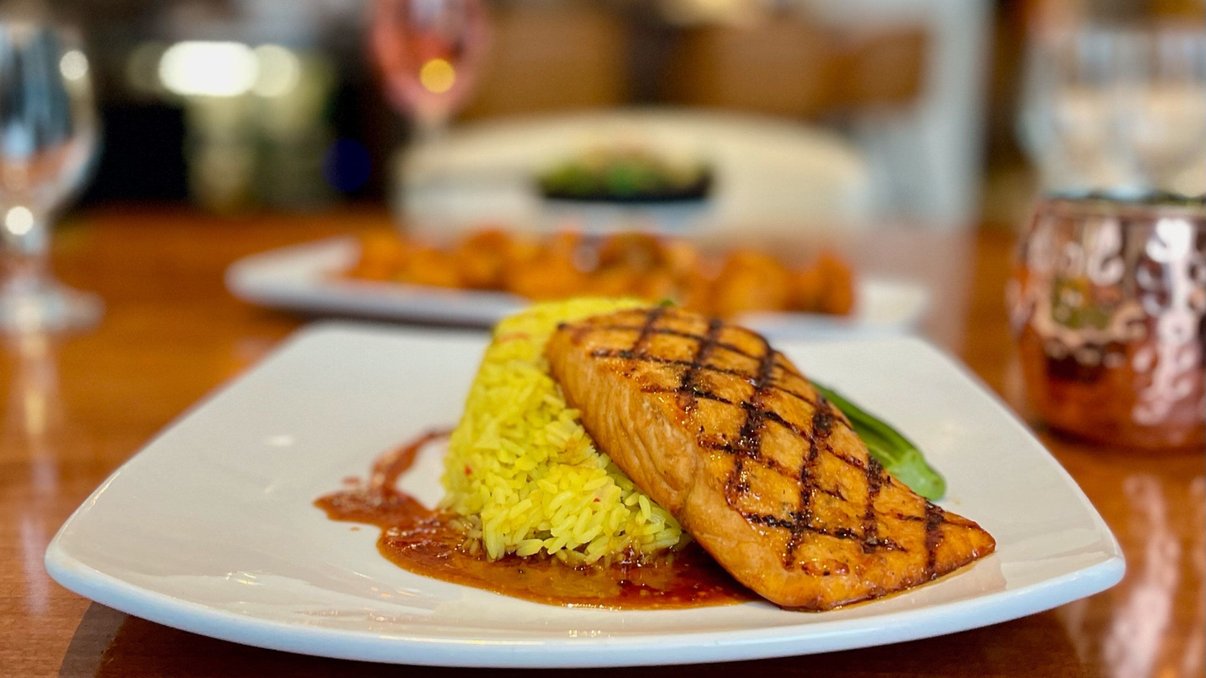 Een bord met gegrilde zalm en gele rijst, vergezeld van saus.