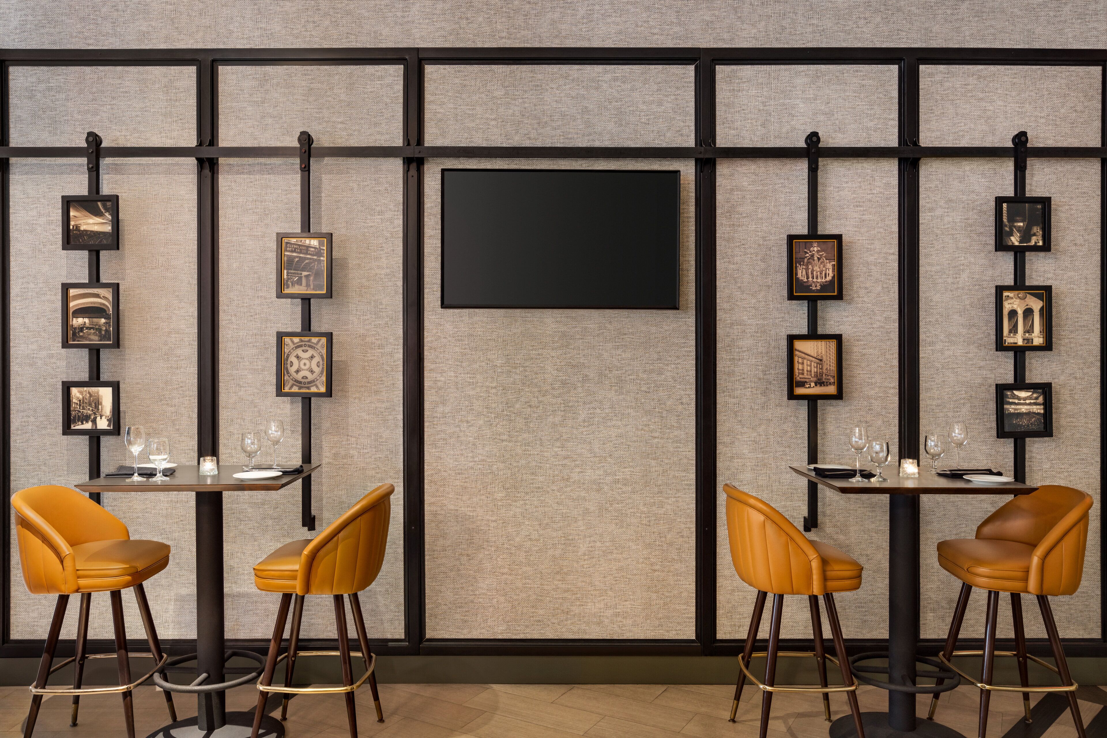 Un espace bar moderne avec deux tabourets, un grand téléviseur à écran plat fixé au mur et des tableaux encadrés qui décorent le mur.