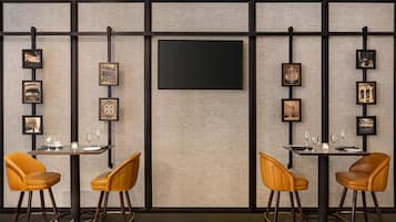 A modern bar area with two bar stools, a large flat-screen TV mounted on the wall, and framed pictures on the wall.