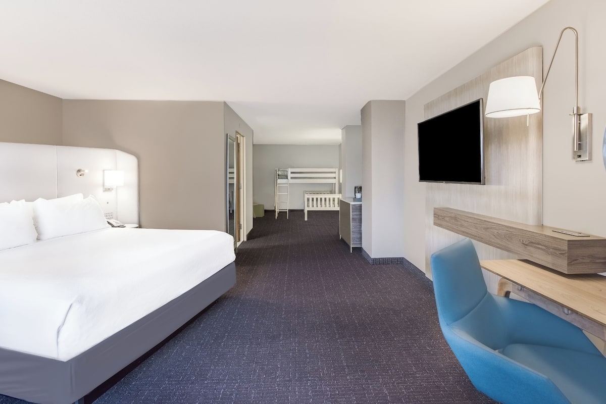 A hotel room with a large bed, a desk with a chair, a TV, and a bathroom with a shower and toilet.