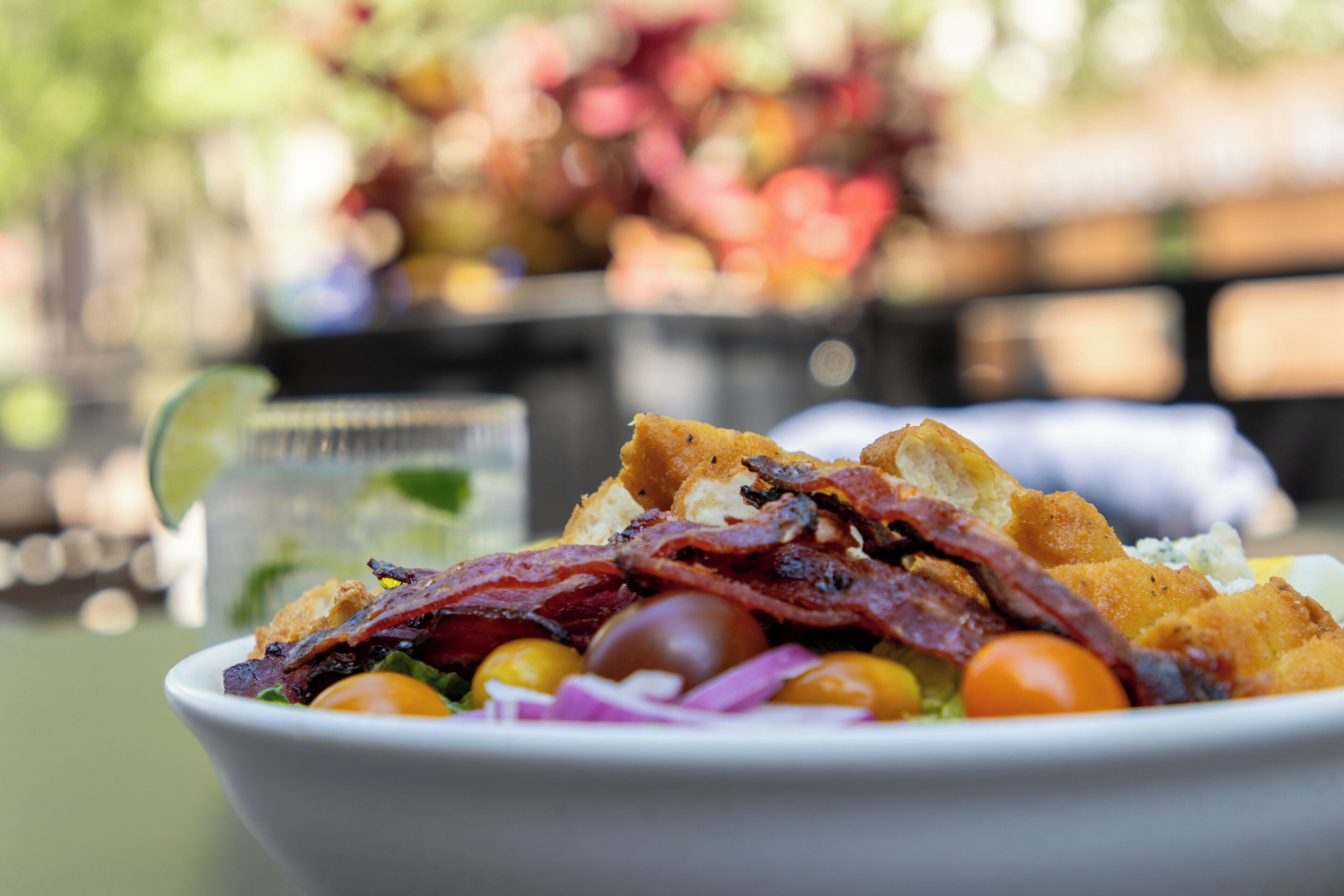 A bowl of salad with various ingredients, including lettuce, tomatoes, and bacon, on a table.