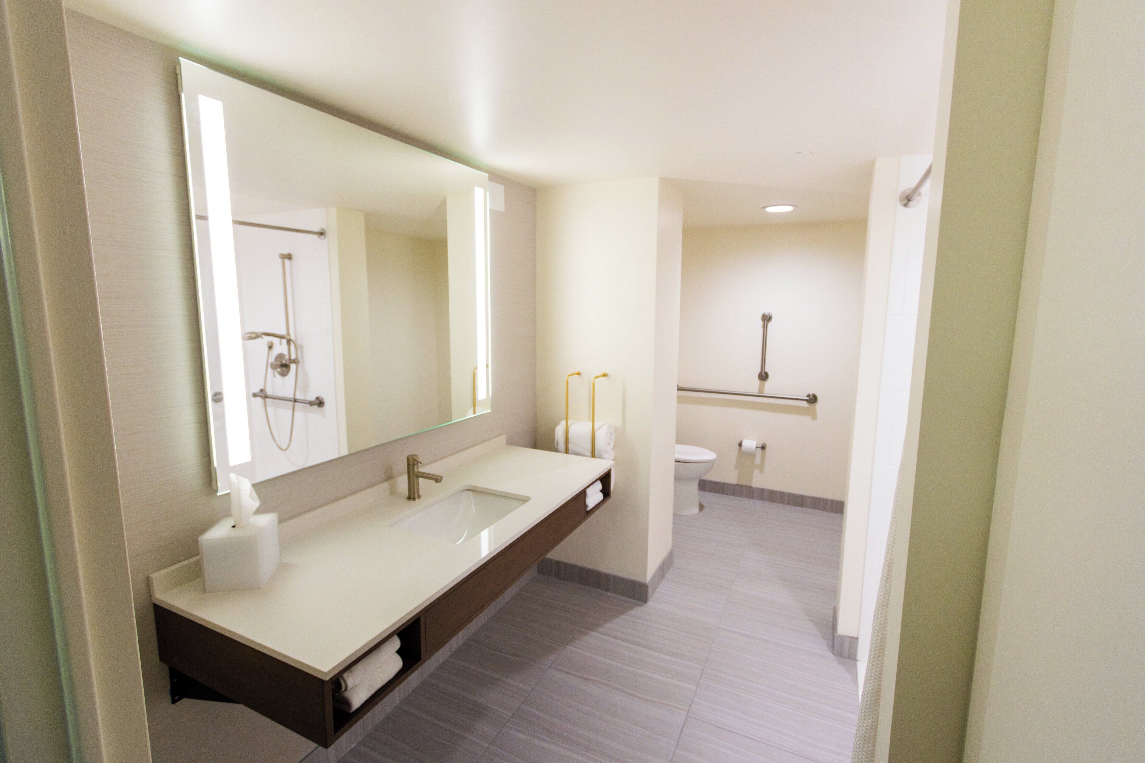 A modern bathroom with a large mirror, two sinks, a toilet, and a shower.