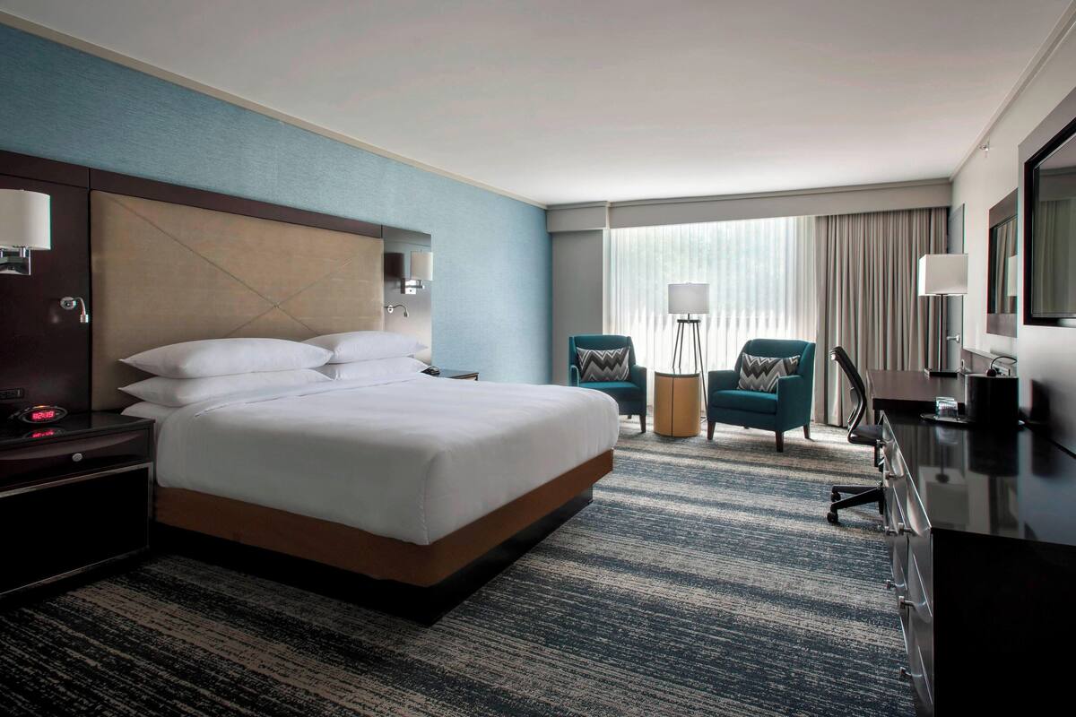 A hotel room with a large bed, a desk, a chair, and a TV.