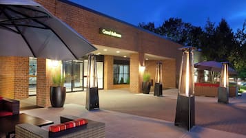 A hotel entrance with a sign reading "Grand Ballroom," outdoor seating with umbrellas, and potted plants.