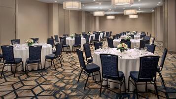A conference room with round tables, blue upholstered chairs, and white tablecloths.