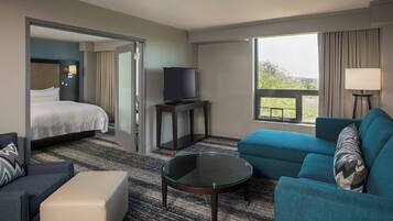 A hotel room with a bed, a TV, a sofa, a coffee table, and a view of the outdoors.