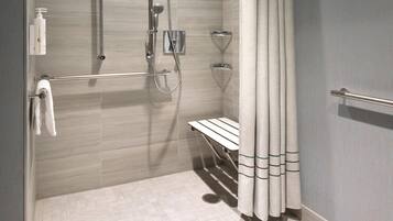 A modern shower area with a handheld showerhead, a wall-mounted faucet, and a bench.