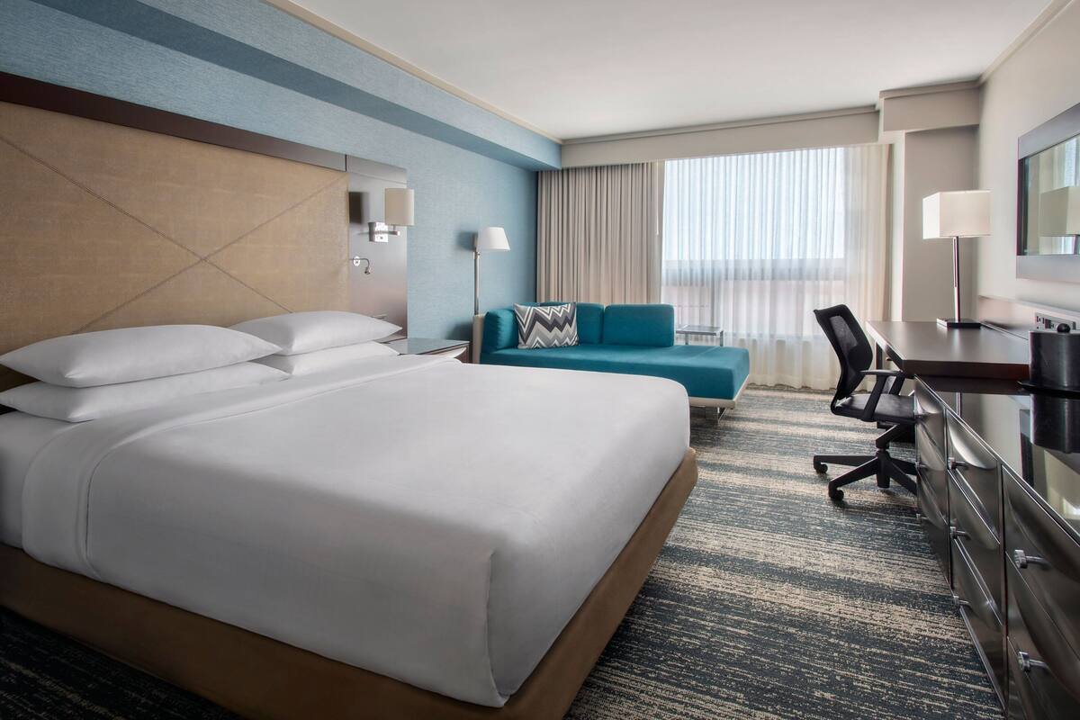 A hotel room with a large bed, a desk, a chair, a sofa, and a TV.