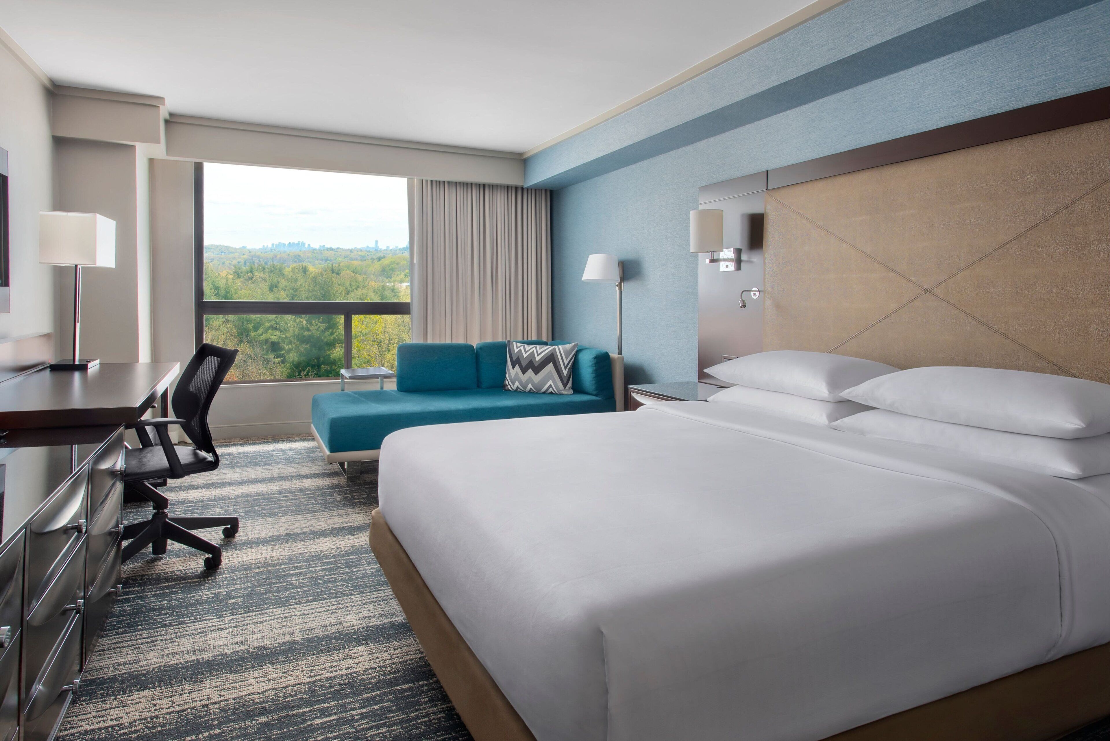 A hotel room with a large bed, a desk with a chair, a sofa, and a view of the outdoors.