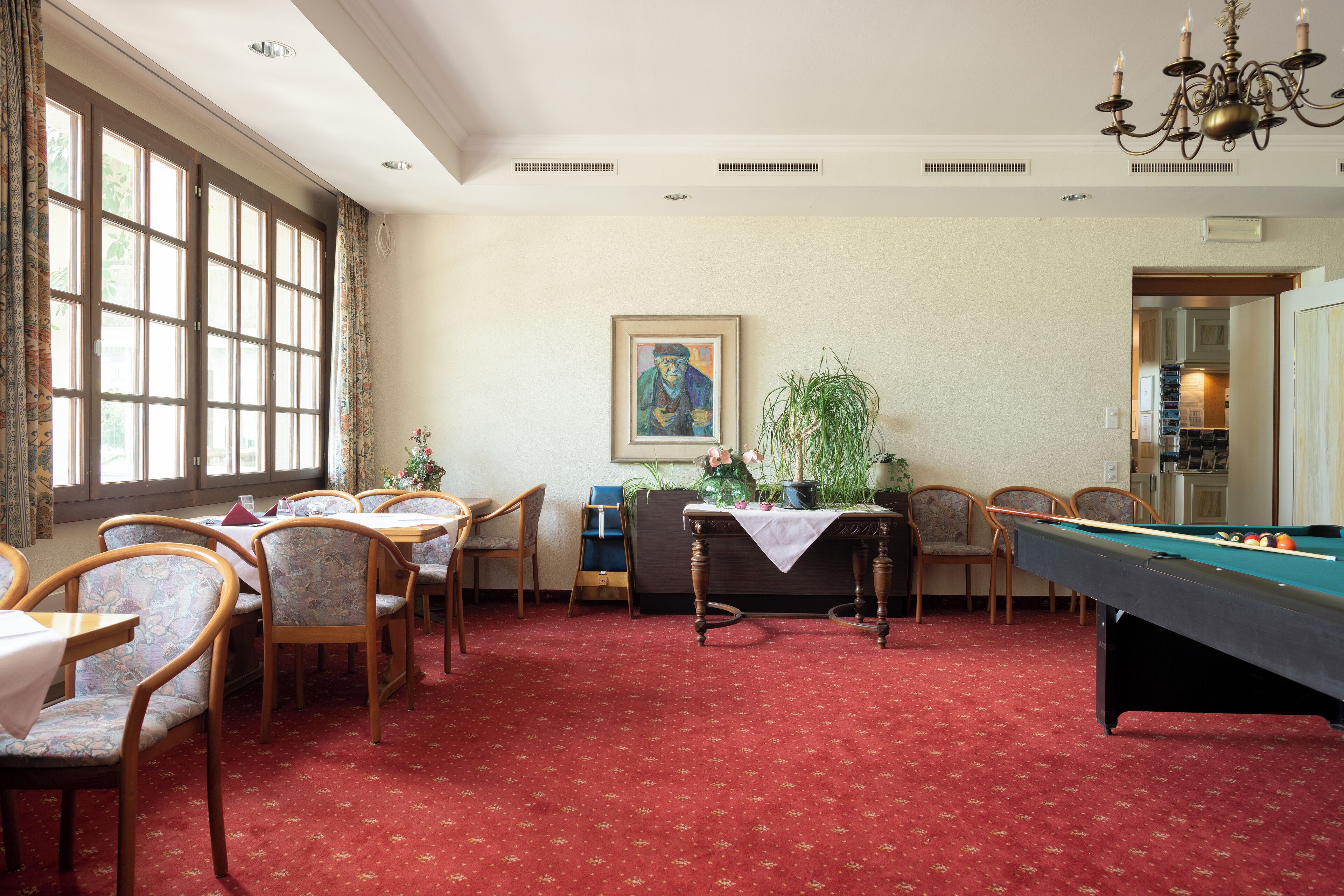 Une pièce comprenant une table de billard, des chaises, une table à manger avec des chaises, une grande fenêtre et un tableau accroché au mur.