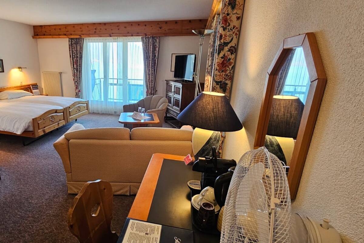 A hotel room with a bed, a sofa, a desk with a lamp, a chair, a small table, and a television.