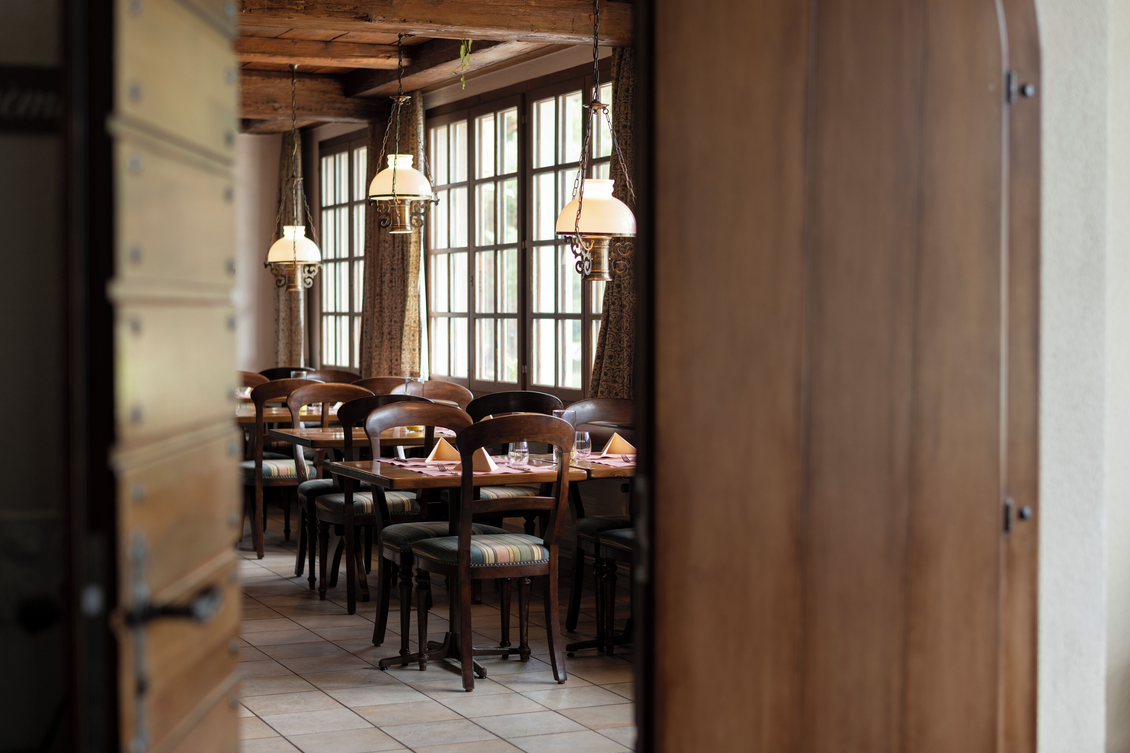 Un comedor con mesas y sillas de madera, lámparas colgantes y amplios ventanales.