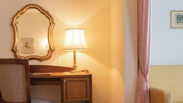 A hotel room with a desk, chair, lamp, and a mirror.
