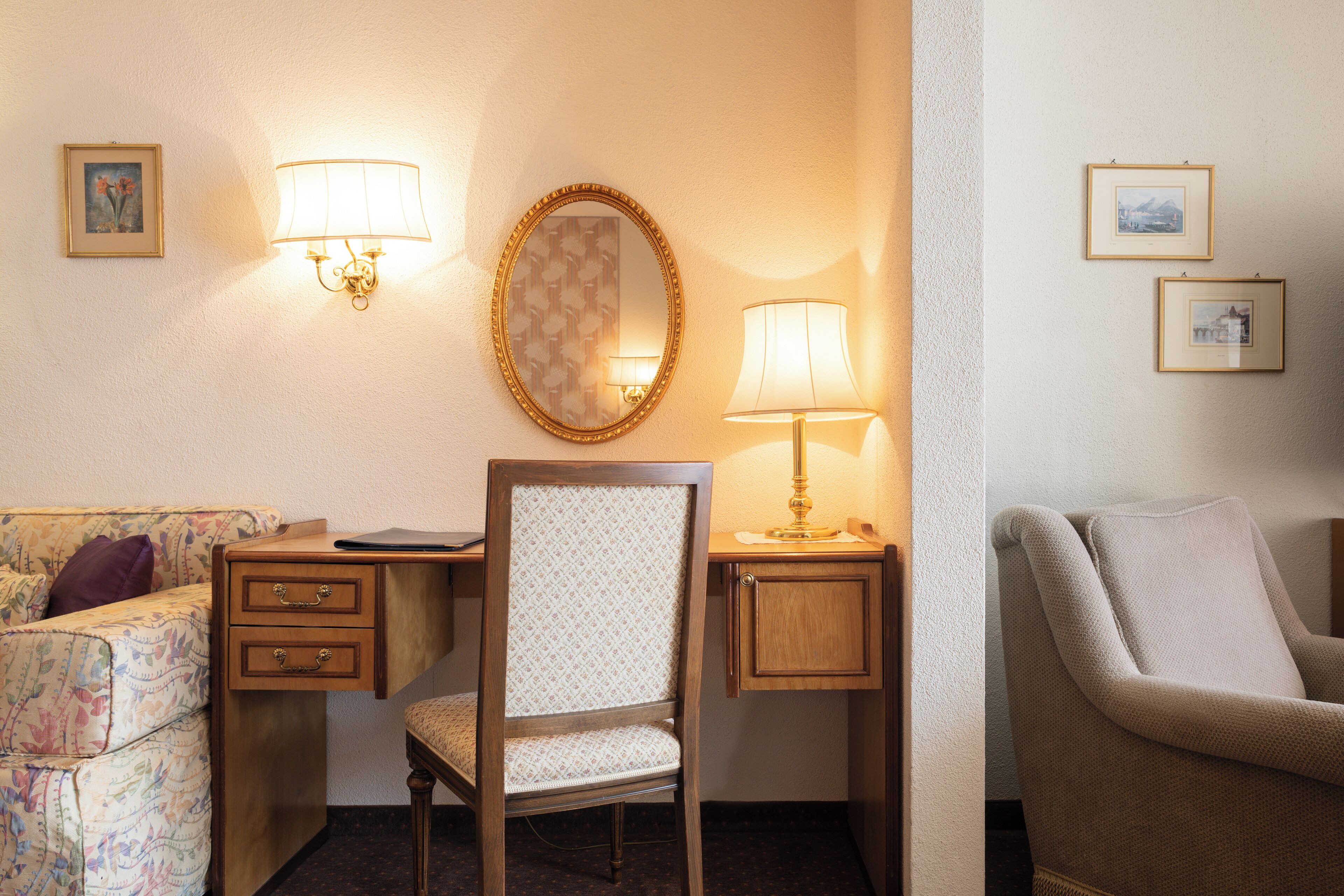 A hotel room with a wooden desk, a chair, a sofa, and a lamp.