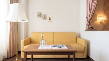 Un sofá amarillo, una mesa de madera con una lámpara, y tres cuadros en la pared.