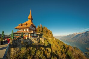 A traditional chalet with a steep roof and a prominent tower, situated on a hillside overlooking a valley and lake. - Seiler au Lac (Boenigen)
