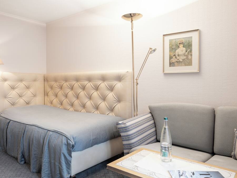 Une chambre d’hôtel avec un lit doté d’une tête de lit capitonnée, un canapé, une lampe sur pied et un tableau encadré au mur.
