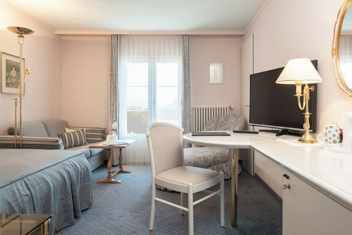 A hotel room with a bed, a desk, a chair, a television, and a lamp.