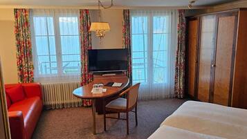 Habitación de hotel con cama, sofá rojo, mesa de comedor con sillas, televisión y armario.