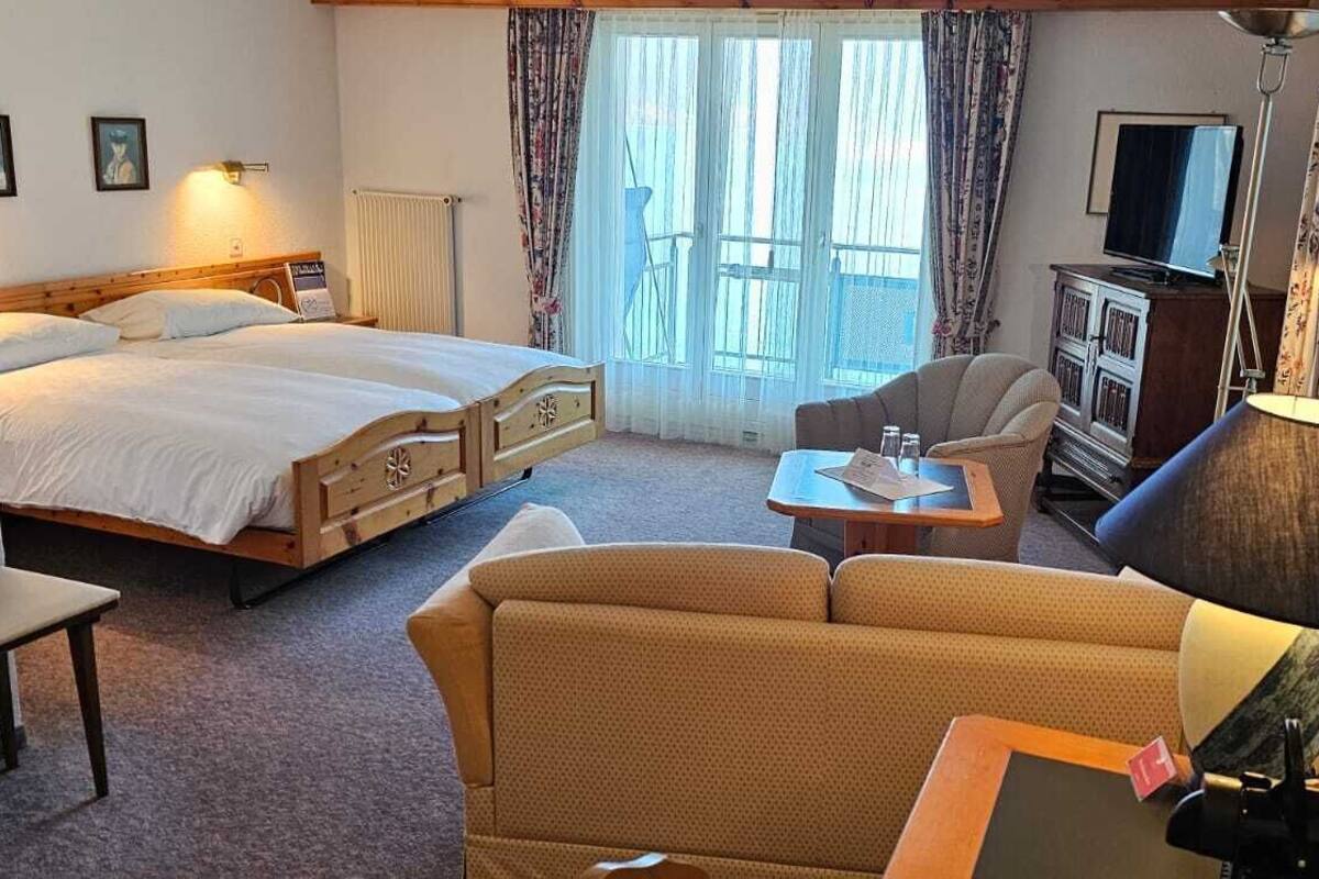 A hotel room with a bed, a sofa, a small table, a lamp, a TV, and a window with curtains.