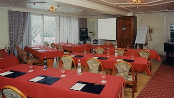 A conference room with multiple tables, each with a red tablecloth, chairs, and wine glasses.