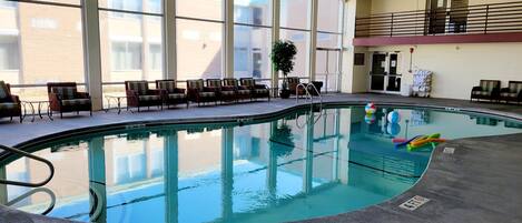 An indoor swimming pool with clear water, surrounded by lounge chairs and large windows.