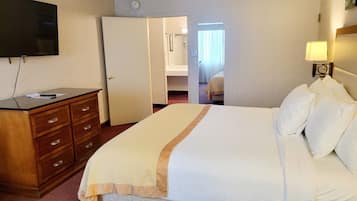 A hotel room with a bed, a dresser, a television, and a door leading to another room.