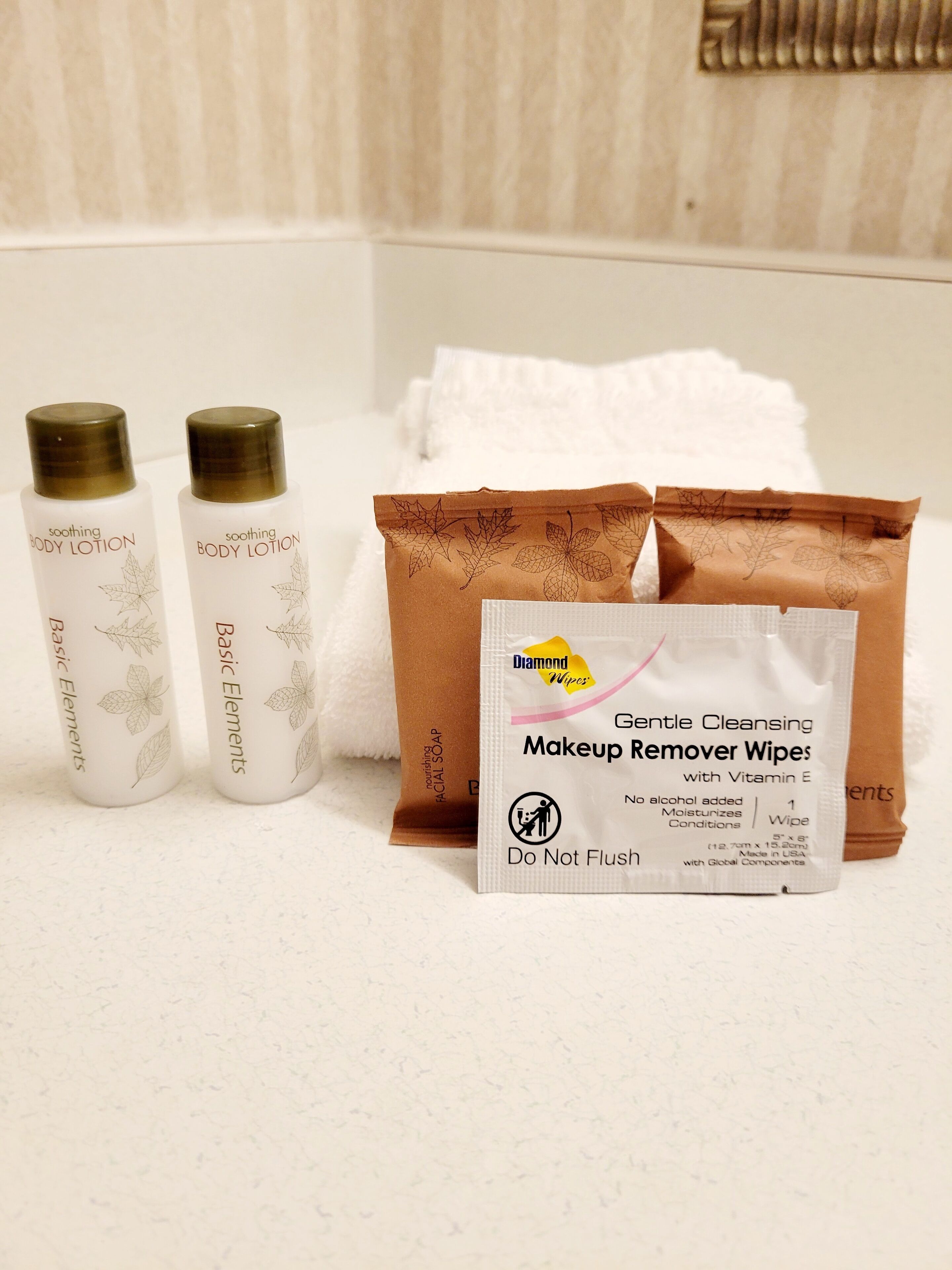 Un baño con encimera blanca, dos botellas de crema corporal relajante, un paquete marrón de jabón facial y un paquete de toallitas Diamond para quitar el maquillaje.