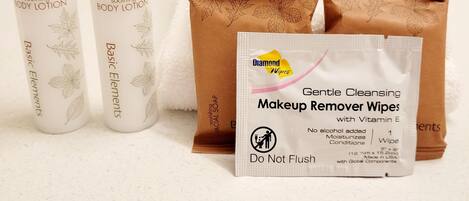 A bathroom with a white countertop, two bottles of soothing body lotion, a brown package of facial soap, and a Diamond wipes makeup remover wipes package.