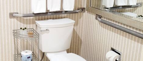 Un baño con inodoro, un cubo de basura, un toallero con toallas dobladas y un espejo.