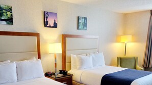 A hotel room with two beds, each with a headboard, a nightstand, a lamp, and a framed picture on the wall. - Bangor Grande (Bangor)