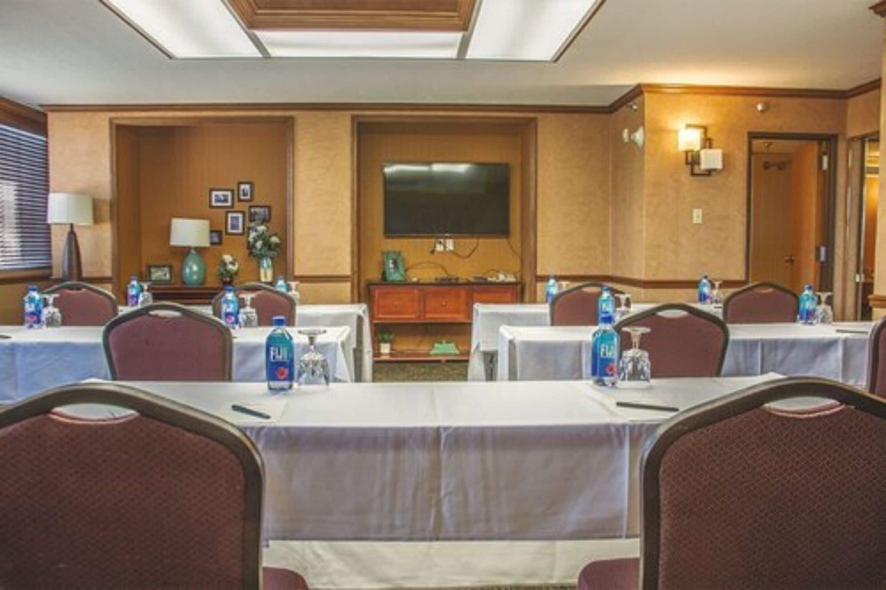 A conference room with tables set up for meetings, equipped with water bottles, and a television screen on the wall.