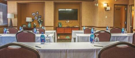 A conference room with tables set up for meetings, equipped with water bottles, and a television screen on the wall.