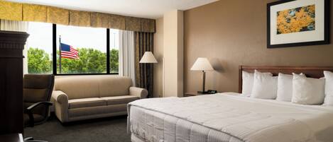 A hotel room with a large bed, a sofa, a desk, and a window with an American flag.