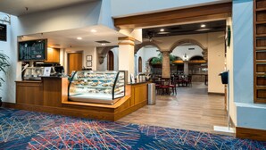 A hotel lobby with a bakery display, seating area, and a coffee machine. - MCM Eleganté Hotel & Conference Center Beaumont (Beaumont)