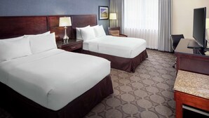A hotel room with two beds, a desk, a TV, and a window with curtains.