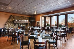 A restaurant with multiple tables, chairs, a stone wall, and large windows.