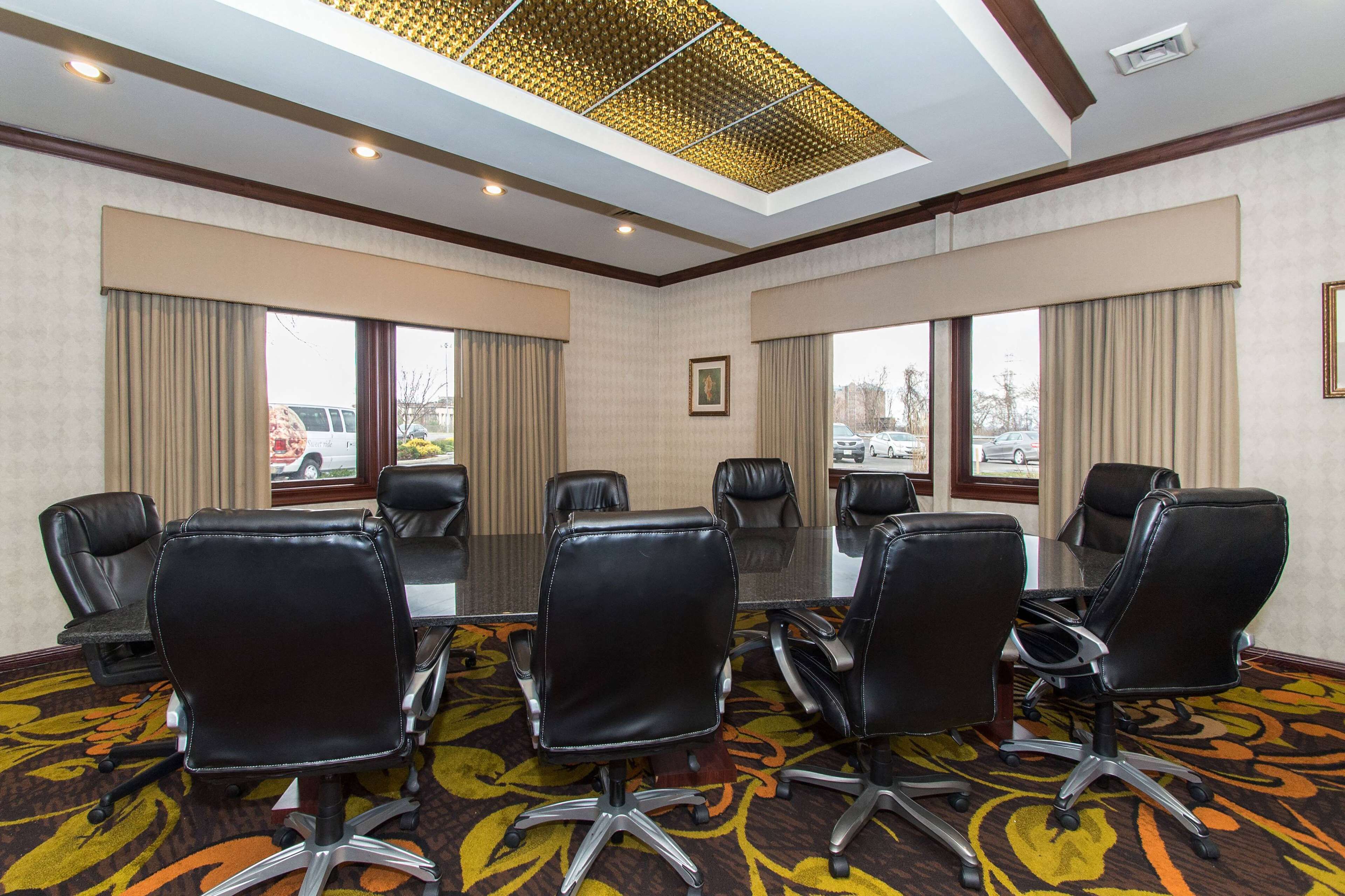 A conference room with a glass table, black leather chairs, and large windows with curtains.