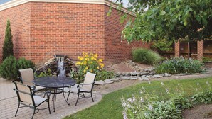 A brick building with a patio area featuring a table and chairs, a small waterfall, and various plants.