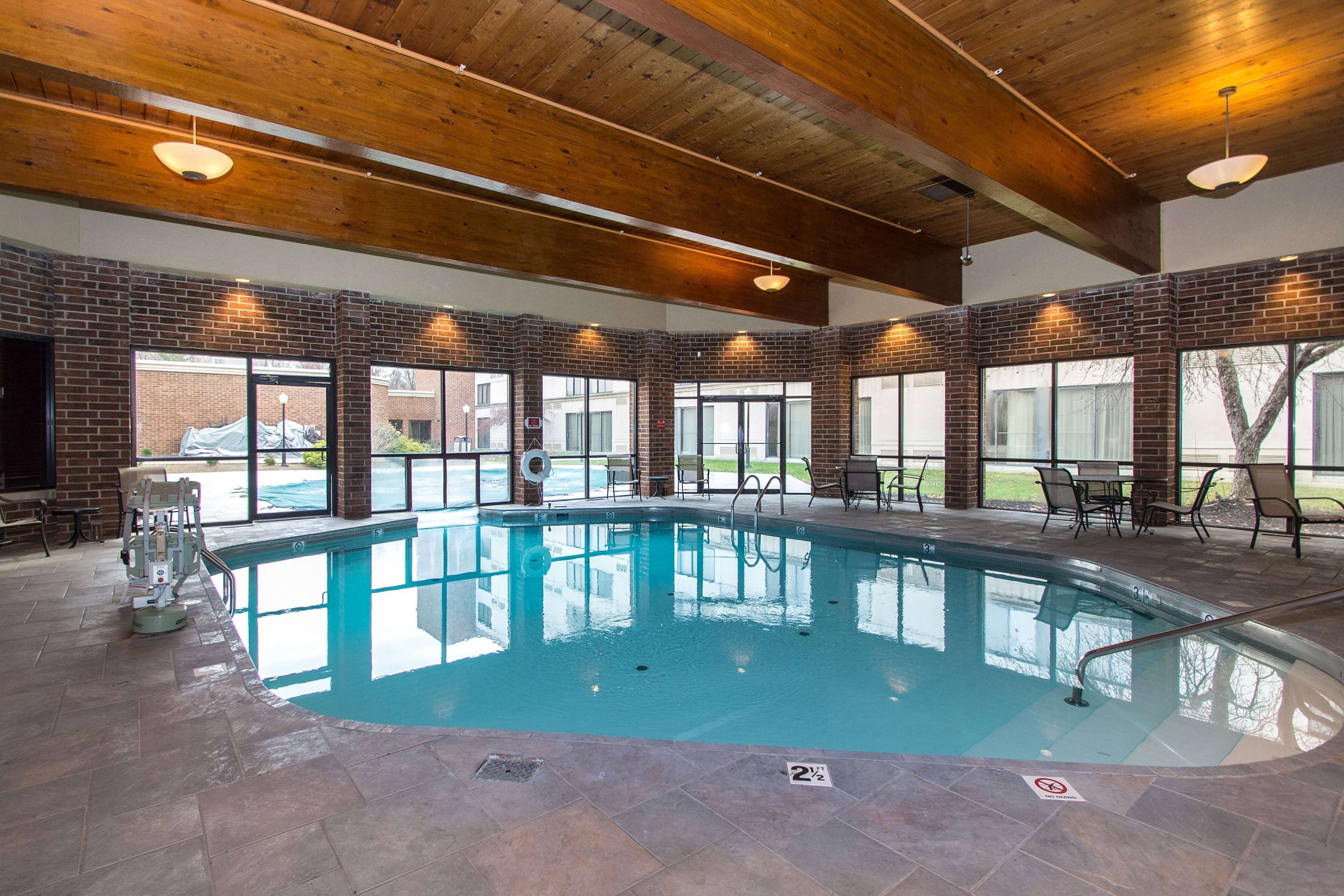 Une piscine intérieure avec un mur en briques, des poutres en bois au plafond et un espace extérieur aménagé pour se détendre.