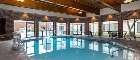 Une piscine intérieure avec un mur en briques, des poutres en bois au plafond et un espace extérieur aménagé pour se détendre.