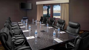 A conference room with a long table, multiple chairs, water bottles, and a TV on the wall.