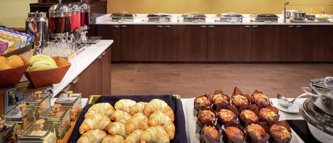 Ein Buffet mit verschiedenen Speisen, darunter Croissants, Muffins und einer Obstschale.